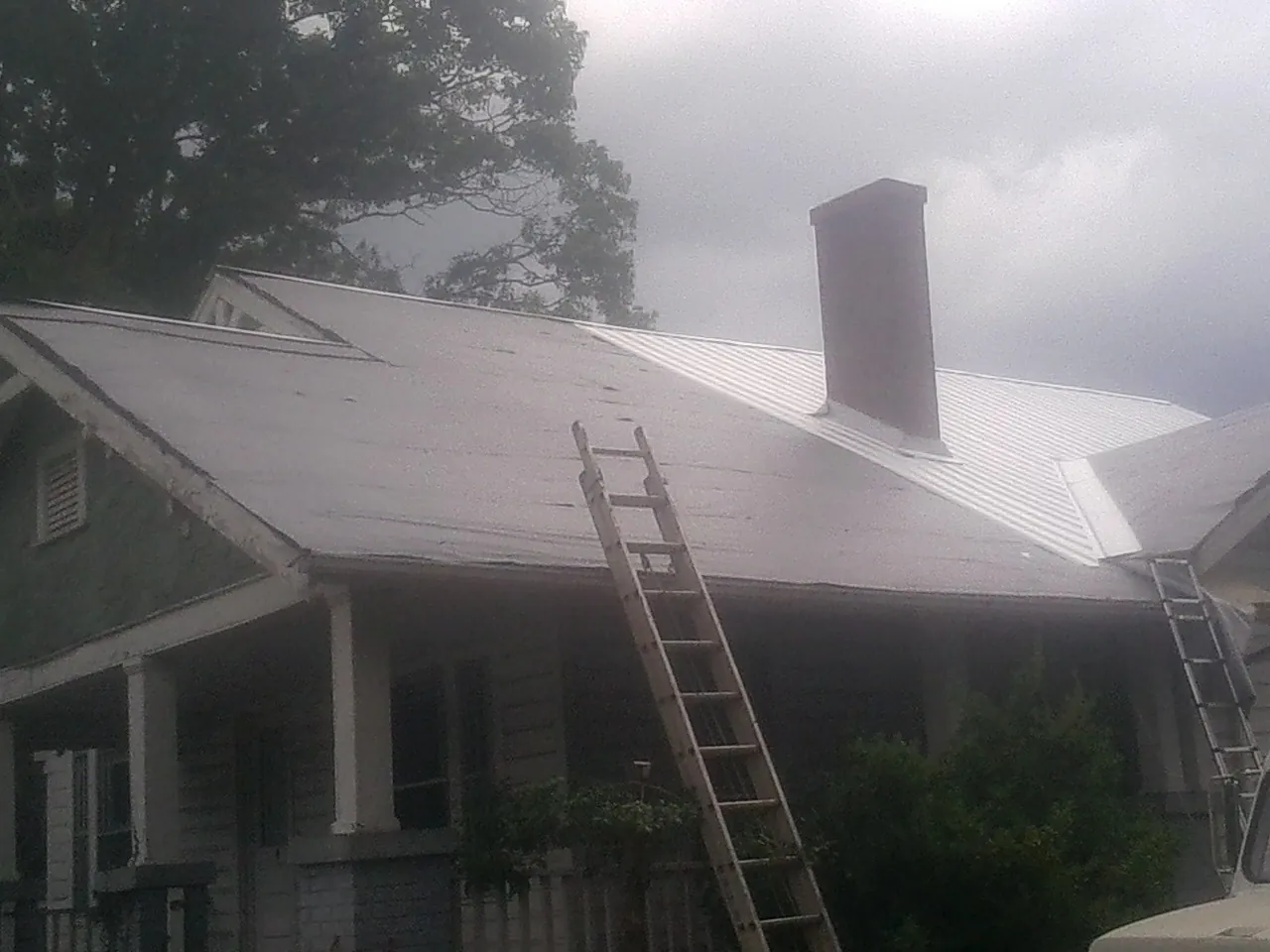 Ladders against a metal roof on an older home with a brick chimney in Colfax